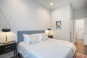 A modern bedroom with a bed, bedside tables, and a wall-mounted light fixture. - 2 Side by Side Homes with Rooftops -Sleeps 24 (Nashville)