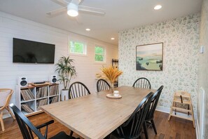 A dining area with a wooden table, black chairs, a white bookshelf with vinyl records, a potted plant, and a painting on the wall. - Spotless Gem | Hot Tub | 15 Min to Broadway (Nashville)