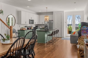 Une cuisine moderne avec des meubles blancs, un îlot central, des tabourets de bar et une table à manger avec des chaises.