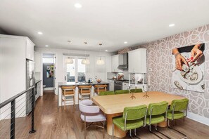A modern kitchen with white cabinets, a wooden dining table, and green chairs. - Mins to Gulch & Broadway | Free Garage + 4.5 Baths (Nashville)