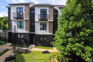 A modern two-story residential building with balconies, a well-maintained lawn, and a tree in the foreground. - Mins to Gulch & Broadway | Free Garage + 4.5 Baths (Nashville)