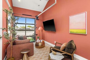 Una habitación con una pared roja, un televisor de pantalla plana, un sofá, una mesita pequeña y una planta en maceta.