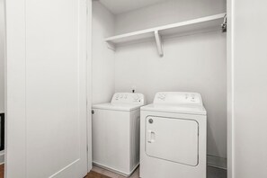 Un cuarto de lavandería con dos lavadoras blancas y un estante encima.
