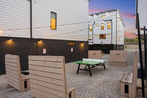 An outdoor patio area with wooden benches and a table, string lights, and a brick floor. - CHARM! Near Broadway in Walkable 8th Ave S! (Nashville)