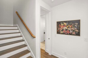 Een trap met houten treden en een leuning, die leidt naar een kamer met witte muren en een bloemschilderij.