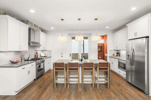 A modern kitchen with white cabinets, a stainless steel refrigerator, and a central island with bar stools. - CHARM! Near Broadway in Walkable 8th Ave S! (Nashville)