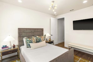 A modern bedroom with a large bed, bedside tables with lamps, a flat-screen TV mounted on the wall, and a bench by the door. - CHARM! Near Broadway in Walkable 8th Ave S! (Nashville)