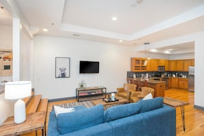 A modern living room with a sofa, coffee table, and a flat-screen TV mounted on the wall. - On Broadway Above Boot Barn (Nashville)