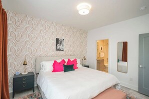 A bedroom with a bed, nightstands, a mirror, and a bathroom door. - 2 Homes-Sleeps 24-Roof Decks-Grills Near Broadway (Nashville)