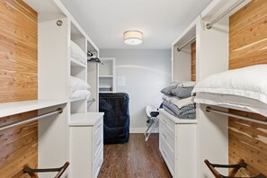 A narrow hotel room with wooden paneling, a bed with white bedding, a small desk with a chair, and a wardrobe with hanging clothes. - Peaceful Nashville Ranch • A Cozy Place to Unwind! (Nashville)