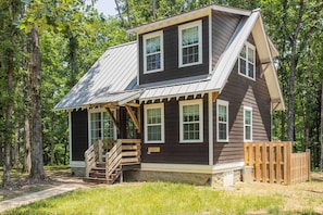 A two-story cabin with a sloped roof, wooden deck, and a small staircase leading to the entrance. - Purple Martin: Secluded Forest Birdwatcher (McEwen)