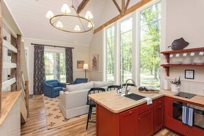 Ein gemütliches Interieur mit einem Essbereich aus Holz, einer Küche mit Holzarbeitsplatte und großen Fenstern mit Blick ins Freie.