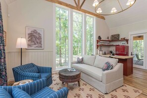 A cozy living room with a sofa, striped armchairs, a round coffee table, and a large window offering a view of trees. - Purple Martin: Secluded Forest Birdwatcher (McEwen)