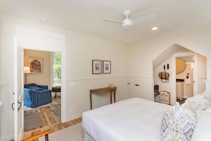 A bedroom with a bed, a desk, a chair, and a small seating area with a sofa. - Purple Martin: Secluded Forest Birdwatcher (McEwen)