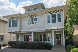 A two-story residential building with a front porch, a flag, and a well-maintained lawn. - Winter Retreat: Hot Tub|Arcade|Near BWAY|Parking (Nashville)