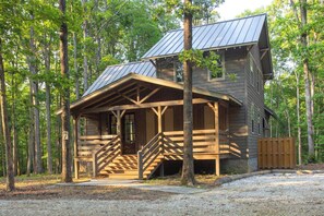 A rustic cabin with a porch, wooden stairs, and a metal roof, surrounded by trees. - The Covey: Luxury Woodland Farm Retreat (McEwen)