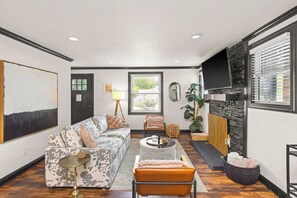 A living room with a sofa, armchairs, a coffee table, a fireplace, and a television. - 1940s Bungalow| Deck+Chef's Kitchen| Dog Friendly (Nashville)