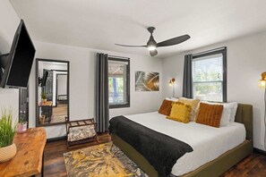 Un dormitorio con una cama, ventilador de techo, televisor y ventana.