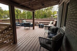 Eine überdachte Terrasse im Freien mit Sitzgelegenheiten und Tischen, eine Ziegelwand und Blick auf Bäume.