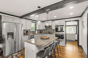 Una cocina moderna con encimeras de granito, electrodomésticos de acero inoxidable y una isla central con taburetes de bar.