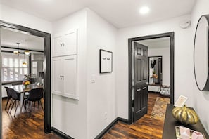 Eine moderne Küche mit weißen Schränken, ein Essbereich mit einem schwarzen Tisch und Stühlen sowie ein Flur mit einer schwarzen Tür und einem gerahmten Bild an der Wand.