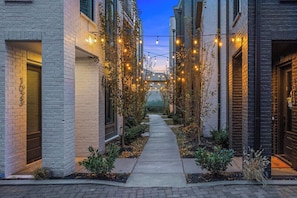 A narrow alleyway with a pathway flanked by buildings with brick facades, string lights, and small plants. - Sleeps 24 | Rooftop Decks Downtown Views (Nashville)