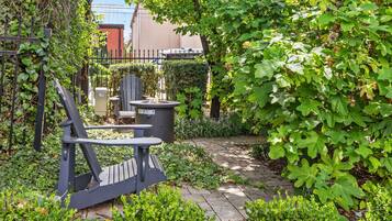 Een tuin met een verhard pad, een bankje en een afvalbak.