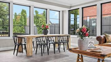A spacious room with large windows, a wooden dining table, black chairs, and a sofa with a decorative pillow.