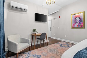 A modern hotel room with a flat-screen TV, a desk with a chair, a potted plant, a patterned rug, and a bed. - The Anthony Suite | Germantown Inn | Breakfast (Nashville)