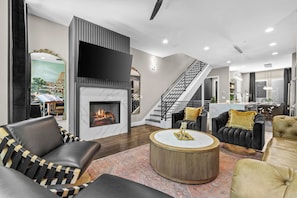 A modern living room with a fireplace, a staircase, and a view of a cityscape. - Karaoke, Rooftop, Fire Pit -The Ryman (Nashville)