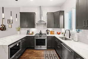 A modern kitchen with dark cabinets, white countertops, a gas stove, and a stainless steel oven. - Gated Luxury in Nashville: Rooftop Views+Fire Pit (Nashville)