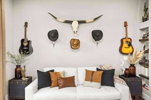 A living room with a white sofa, two guitars, and a large bull skull on the wall. - Gated Luxury in Nashville: Rooftop Views+Fire Pit (Nashville)