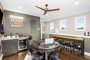 A modern kitchen with a bar area, wooden ceiling fan, and a sign reading "BOURBON BEER WHISKEY". - Gated Luxury in Nashville: Rooftop Views+Fire Pit (Nashville)