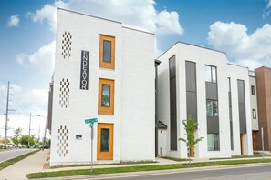 Ein modernes Gebäude mit heller Fassade, drei Fenstern und einem Straßenschild.