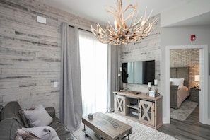 A modern living room with a wooden wall, a large flat-screen TV, a wooden coffee table, and a sofa. - Downtown Lux Condo: South Belle (Nashville)