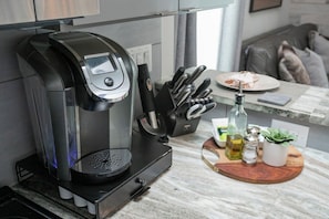 A modern kitchen with a coffee maker, a knife block, and a wooden cutting board with condiments. - Downtown Lux Condo: South Belle (Nashville)
