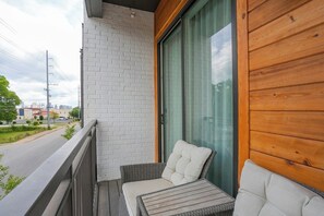 Ein Balkon mit einem Korbsessel, einem Tisch, einer weißen Backsteinmauer und Blick auf die Straße.