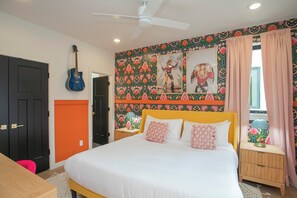 Una camera da letto con un letto, una chitarra, una ventola a soffitto e una parete con motivi floreali.