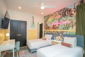 Un dormitorio con dos camas, un escritorio, una silla, un televisor y un mural.