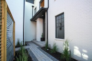 A modern building with white brick walls, a wooden door, and a paved pathway with plants. - Bohemian Chic Hot Tub Sleeps 12 (Nashville)