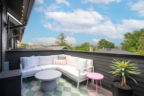 A rooftop patio with a white sofa, a round table, a small pink table, and a potted plant. - Bohemian Chic Hot Tub Sleeps 12 (Nashville)