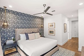A modern bedroom with a tufted headboard, a ceiling fan, a patterned wallpaper, and a bed with white bedding. - 2 Homes-Sleeps 24 | Downtown Great for Big Groups! (Nashville)