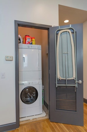 A laundry room with a front-loading washer and dryer, a drying rack, and cleaning supplies. - On Broadway: 2 Lofts Sleep 12 (Nashville)