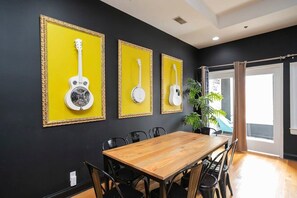 Ein Essbereich mit einem Holztisch und schwarzen Stühlen, vor einer schwarzen Wand mit drei gerahmten Gitarren.