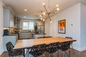 A modern kitchen with a wooden dining table and black chairs, a chandelier, and a poster on the wall. - Near Broadway - Walk to Geodis Park + WeHo (Nashville)