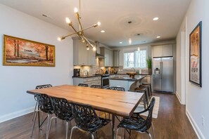 Cozinha moderna com mesa e cadeiras de madeira, eletrodomésticos de aço inoxidável e luminária pendente.