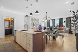 A modern kitchen with a central island, pendant lighting, and a dining area with a sofa and chairs. - Nash Skyline Views Rooftop with Fire Pit  Grill (Nashville)