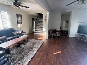 A spacious living room with a dark wood floor, a leather sofa, a coffee table, and a TV. - Dual Purpose Comfort: 4BR Park & Beach House + Office & High Speed WiFi (Kawartha Lakes)