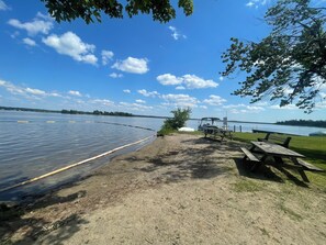 A lakeside picnic area with a boat dock, picnic tables, and a grassy path. - Dual Purpose Comfort: 4BR Park & Beach House + Office & High Speed WiFi (Kawartha Lakes)