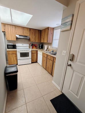 A compact kitchen with wooden cabinets, a microwave, stove, and a trash bin. - Parkside Paradise (Inverness)